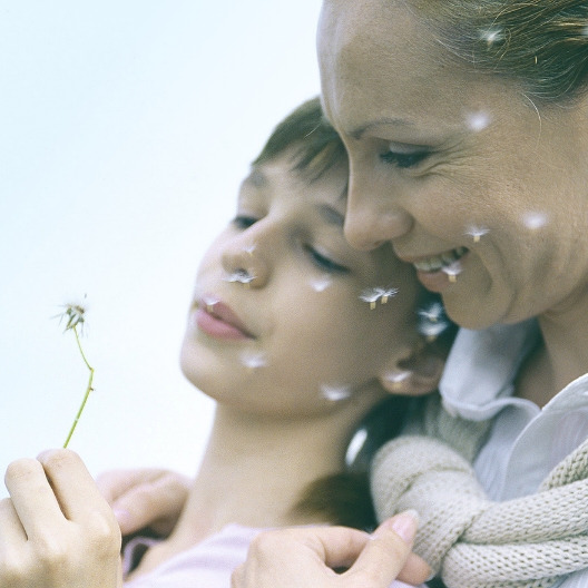 Mother and her child sitting and blowing on a dandelion